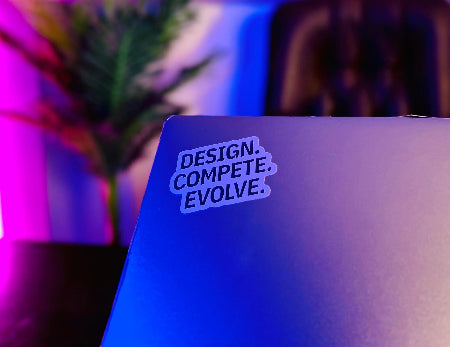 Laptop with a sticker reading 'Design. Compete. Evolve.' on a blurred background